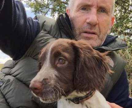 Close up photo of a man with a brown and white dog sitting next to him