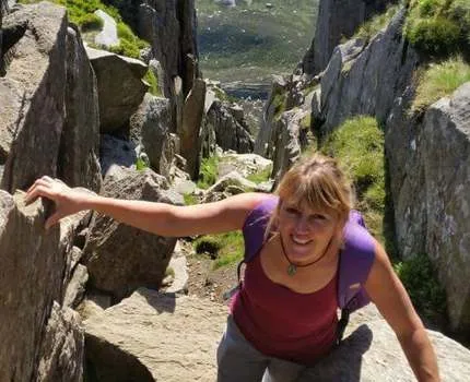 Photo of a woman wearing a purple t-shirt, outdoors climbing rocks