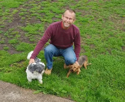 Photo of a man kneeling on the grass with two dogs next to him